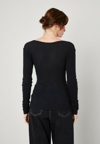 Crna majica dugih rukava s okruglim izrezom, prilagođenog dizajna, mekog tekstura i nabranim rukavima, uparena s tamnim trapericama.