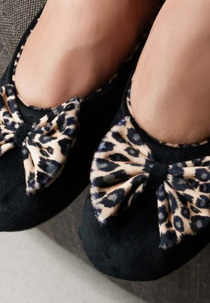 Ballerines noires en daim doux avec un détail de nœud à imprimé léopard. Les chaussures ont un bout rond et une texture lisse.