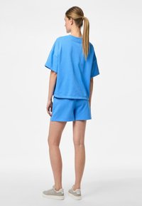 Tricou scurt din bumbac de un albastru deschis, asortat cu pantaloni scurți. Textura este netedă, iar designul are o croială lejeră și guler rotund.
