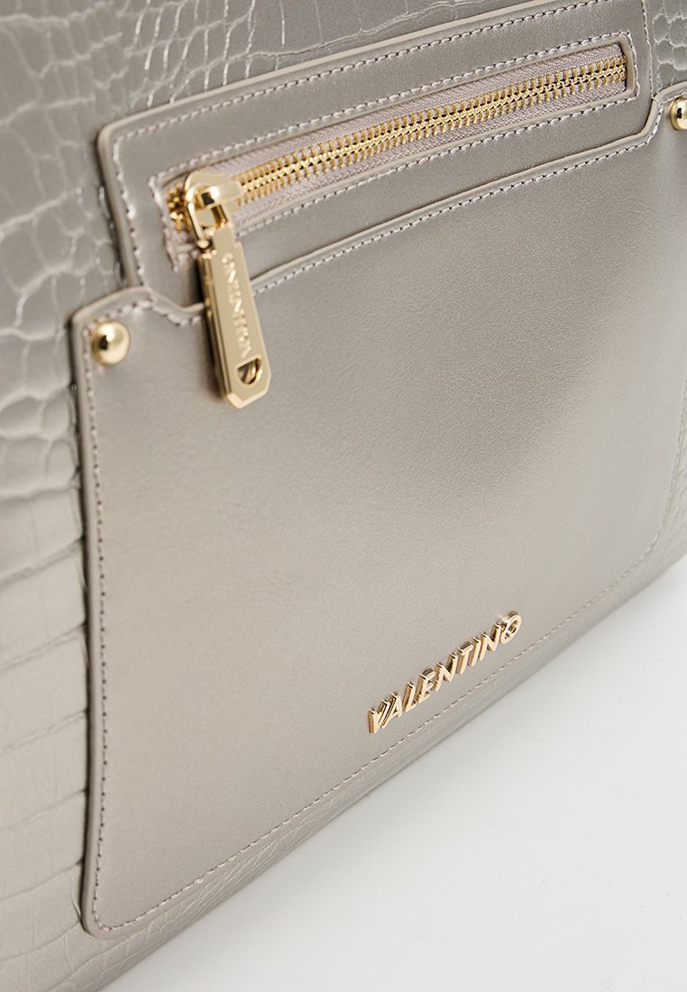 Sac à main en simili cuir gris avec un motif crocodile texturé, doté d'une poche zippée dorée et d'un détail de logo métallique à l'avant.