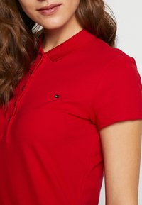 Czerwona koszulka polo wykonana z bawełny, z krótkimi rękawami, klasycznym kołnierzykiem i zapięciem na guziki. Posiada małe logo na piersi.