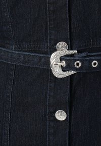 Robe en denim foncé avec une boucle de ceinture argentée, présentant une finition texturée et un motif décoratif sur la boucle. Accent de bouton argenté.