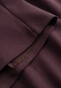 Gros plan de tissu violet foncé montrant un ourlet replié avec des coutures visibles et un travail de couture détaillé.