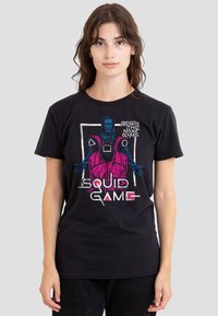 Black t-shirt featuring a colorful graphic with characters from "Squid Game." The design includes bold text and vibrant colors against a dark background.