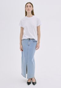 Bela bomba majica iz bombaža kombinirana z svetlo modrim denim maxi krilom z razporkom spredaj. Črne čevlje z ostrim nosom dopolnjujejo videz.