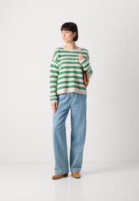 Maglione a righe in crema e verde, abbinato a jeans a gamba larga blu chiaro. Una borsa marrone e calzature casual completano l'outfit.