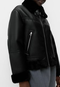 Zwarte leren jas met een bontkraag, ritssluiting aan de voorkant en een zijzak. Heeft een cropped ontwerp en een zachte, gestructureerde stof aan de zoom en manchetten.