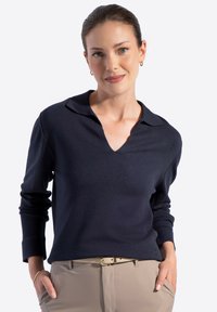 Navy blue pulower z dekoltem w serek i długim rękawem, wykonany z miękkiego materiału. Charakteryzuje się luźnym krojem i subtelną teksturą. Beżowe spodnie z paskiem.
