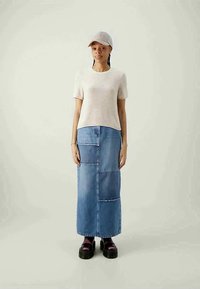 Top de malha bege de manga curta, combinado com uma saia longa de denim claro com secções em patchwork. Usado com sapatos plataforma pretos chunky e um boné claro.
