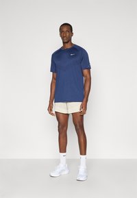 Ναυτικό κοντομάνικο μπλουζάκι Nike με υφή, συνδυασμένο με ανοιχτό μπεζ σορτς και λευκά αθλητικά παπούτσια. Απλή, αθλητική εφαρμογή.