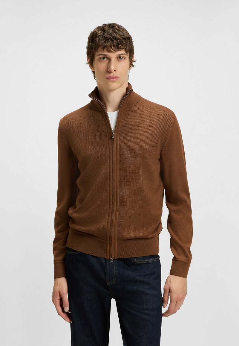 Maglione marrone con zip, in maglia strutturata, colletto alto e polsini aderenti, abbinato a jeans scuri. Tessuto morbido con una vestibilità casual.