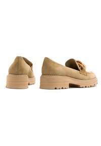 Beżowe zamszowe buty na grubym obcasie, z zapinaniem na sznurowadła i gumową podeszwą. Widoczne detale tekstury i przeszycia.