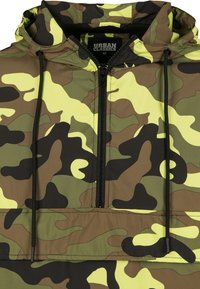 Camo-mönstrad huva jacka i gröna, gula och bruna toner. Har en kvartdragkedja, snoddar och en avslappnad passform.