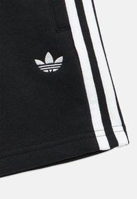 Μαύρο ύφασμα με λευκό λογότυπο Adidas trefoil και δύο κάθετες λευκές πλευρικές ρίγες, μέρος του τμήματος του ποδιού ενός ενδύματος.