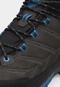 Detailní záběr černé a šedé turistické boty s modrými akcenty, černými tkaničkami s reflexními puntíky a texturovaným geometrickým vzorem na svršku.