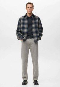 Károvaná flanelová košeľa v tmavomodrej a béžovej farbe, kombinovaná s námorníckym sveterom, svetlošedými nohavicami a čiernymi topánkami. Hladká textúra, uvoľnený strih.