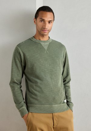Green sweatshirt with a textured fabric, crew neck, and ribbed cuffs. Features a small label at the hem and a relaxed fit. Design is simple and functional.