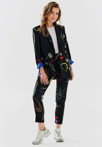 Czarny garnitur z kolorowymi wzorami kwiatowymi w neonowych odcieniach. Niebieskie mankiety w marynarce; dopasowane spodnie. Połączony z jasnoszarymi trampkami.