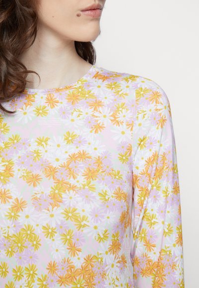 Blusa de mangas longas com padrão floral, apresentando flores vibrantes em laranja, amarelo e branco sobre um fundo rosa claro. Textura de tecido suave e lisa.