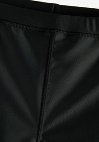 Shorts de bain noirs en matériau lisse, dotés d'une ceinture solide et de coutures plates pour le confort et la durabilité.