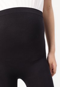 Leggings de maternidad negros con cintura alta, hechos de un material suave y elástico. Textura lisa y diseño ajustado sin patrones ni herrajes.