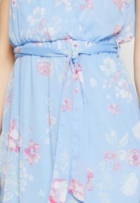 Ljusblå klänning med blommönster i rosa och vitt, med en knytning vid midjan och en mjuk, flödande tygetextur.