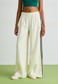 Calças largas brancas com riscas laterais pretas e uma cintura elástica, emparelhadas com sapatos brancos de slip-on. Material suave e leve.
