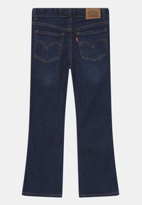 Jeans de mezclilla azul oscuro en corte acampanado con una cintura de altura media, dos bolsillos traseros con detalles de costura y una etiqueta de marca de cuero en la cintura.