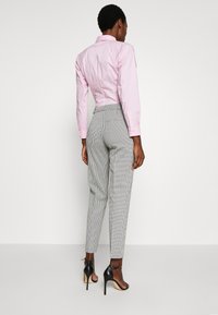 Camicia fitted rosa chiaro con maniche lunghe, abbinata a pantaloni a righe grigie e bianche. Sandali neri con tacco alto completano l'outfit.