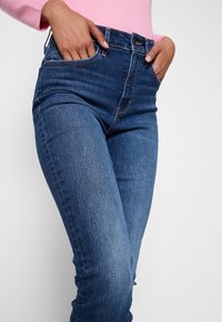 Modré džínové kalhoty s úzkým střihem, pěti kapsami a středně vysokým pasem. Materiál má hladkou texturu s jemným vyblednutím.