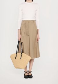 Beige wikkelrok met een strik in de taille, witte top met lange mouwen, geweven stro-tas met zwarte handgrepen en zwarte crisscross-schoenen.