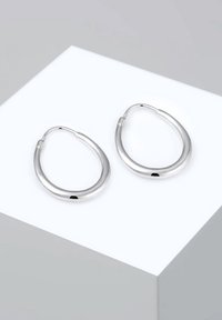 Paire de boucles d'oreilles anneaux en argent lisse et poli avec une forme ovale légèrement aplatie, présentées sur une surface blanche.