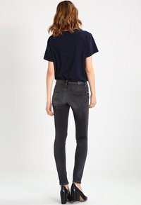 Parte superior de marina de mangas cortas combinada con unos jeans ajustados en negro desgastado y zapatos de tacón negros. Vista trasera que muestra la silueta del atuendo.