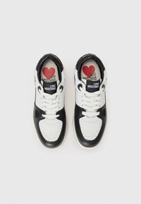 Witte en zwarte leren sneakers met vetersluiting, geperforeerde teen en "LOVE MOSCHINO" branding op de tong en binnenzolen. Rode hartdetail binnenin.