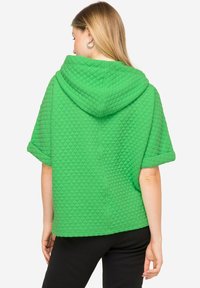 Felpa verde trapuntata con un grande cappuccio e maniche corte. Presenta un motivo a diamante testurizzato, con una vestibilità relax e uno stile casual.