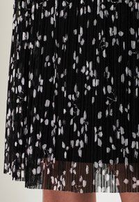 Kladěná černá sukně s květinovým vzorem v bílé barvě. Průhledná textura na lemu, s vrstveným efektem.