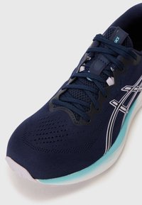Scarpa da corsa navy con tomaia in mesh, dettagli testurizzati e logo bianco a contrasto. Presenta una linguetta imbottita e una suola di un leggero colore menta.