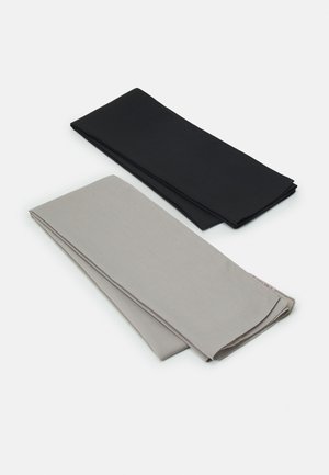 Deux morceaux de tissu pliés : un noir et un gris clair. Tous deux ont une texture lisse et une forme rectangulaire, avec des bords de couture visibles.
