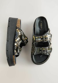Sandalias de plataforma negras con adornos de cuentas metálicas decorativas y dos correas con hebillas. Plantilla de corcho con una suela de goma negra texturizada.