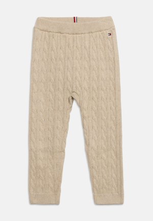 Beige kabelstrikkede bukser med ribbet linning og manchetter, lille logo nær linningen og trikolor stribe detalje på linningen.