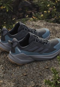 Graue Wanderschuhe mit einem strukturierten Obermaterial, blauen Akzenten und einer robusten Sohle. Enthält das Adidas Terrex-Branding an der Ferse.
