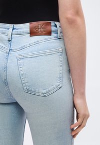 Φωτεινά γαλάζια τζιν Calvin Klein σε άτομο που φοράει μαύρο τοπ, εμφανίζοντας την πίσω τσέπη και την καφέ δερμάτινη ετικέτα της μάρκας στη ζώνη μέσης.