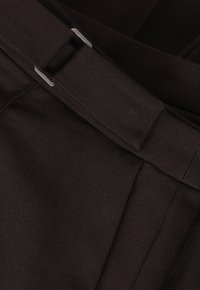 Gros plan d'une ceinture en tissu noir avec une boucle rectangulaire argentée passée à travers un vêtement noir assorti.