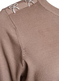 Bežový pletený svetr s kulatým výstřihem, ribbed texturou a dvěma stříbrnými ozdobnými mašlemi na ramenech.