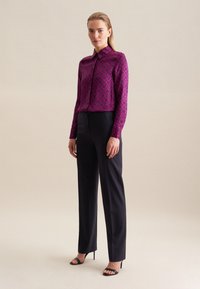 Blusa viola a fantasia con colletto, abbinata a pantaloni neri sartoriali e sandali neri con tacco. Tessuto liscio con design geometrico.