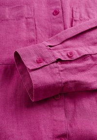 Långärmad magenta linne skjorta med knäppte ärmslut och synliga sömnadsdetaljer på tygstrukturen.