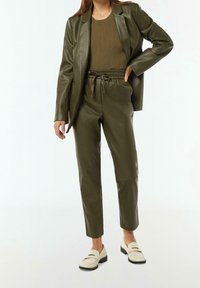 Blazer en cuir synthétique vert olive et pantalon assorti avec une taille élastique. Top côtelé vert olive en dessous et mocassins crème complètent la tenue.