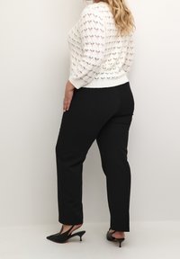 Kremliger Strickpullover mit offenem Maschenmuster und Dreiviertelärmeln, kombiniert mit schwarzen geraden Hosen und schwarzen spitzen Slingbacks.