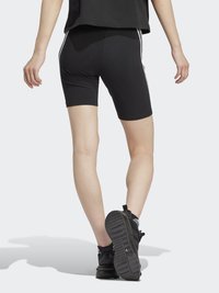 Shorts atletici negri, cu o croială ajustată, având dungi laterale albe. Purtați cu un top negru lejer și încălțăminte sport neagră cu talpă texturată.