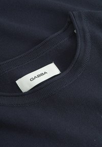 Tmavě modrá pletenina s kulatým výstřihem. Na bílém štítku je uvedena značka "GABBA". Povrch je hladký s jemnými detailem šití.